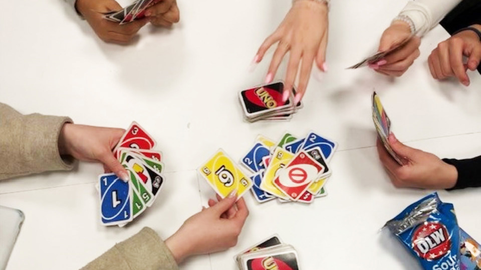 Man ser händer från fyra personer som sitter och spelar kortspelet Uno runt ett bord.