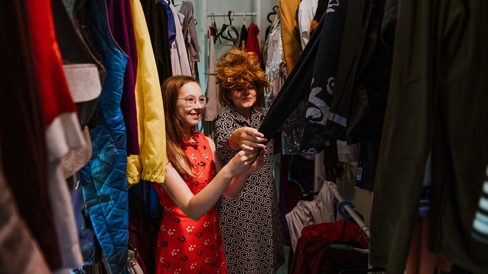 Två barn i en stor garderob fylld med utklädningskläder.