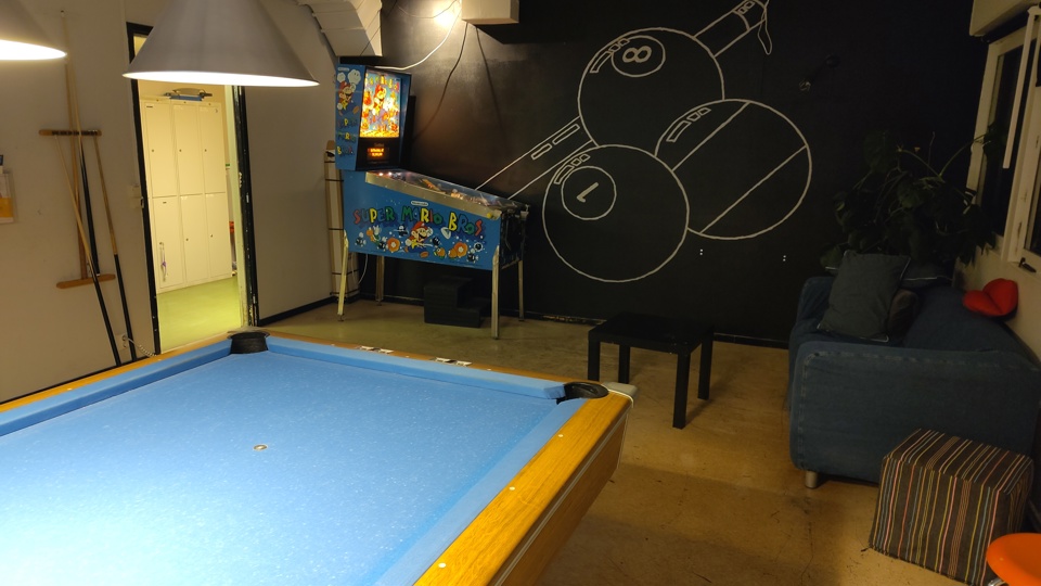 Ett rum med biljardbord, flipperspel och en soffa.