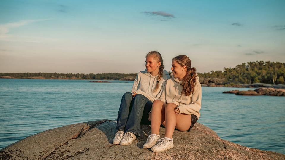 Två barn sitter på en klippa i kvällssolen.