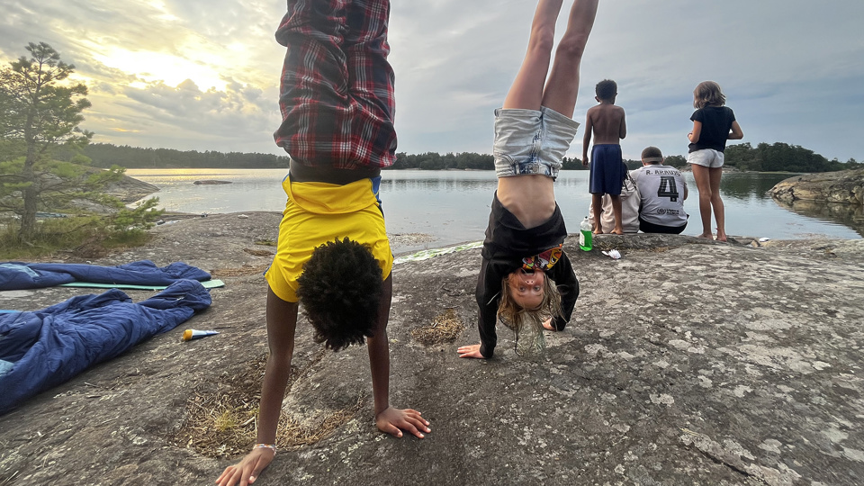 Två barn står på händer på en klippa vid vattnet.