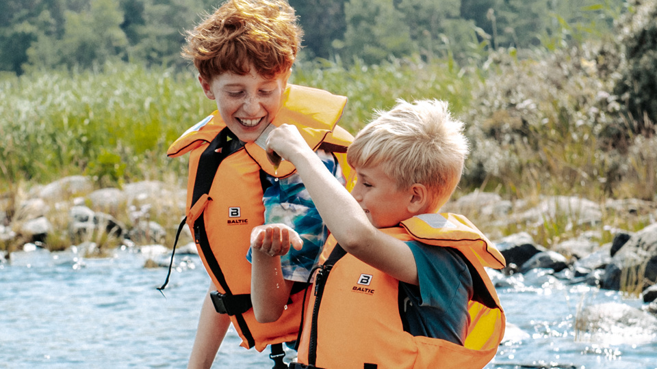 Två barn sitter på en sten i vattnet och leker med vattendroppar.