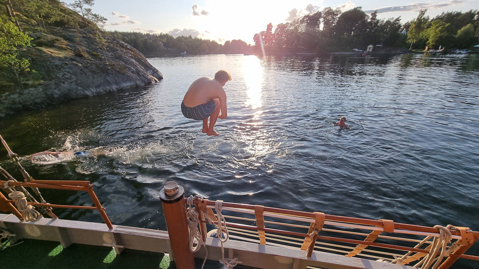 En pojke hoppar i vattnet från ett segelfartyg.