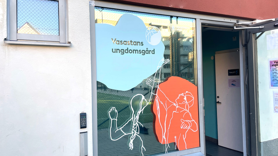 Fönster med namnet på verksamheten och färgglada motiv, foto.