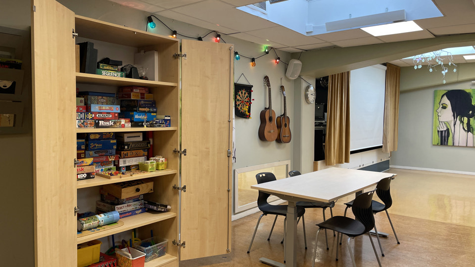 Spelhörna med sittplatser vid bord, brädspel i en hylla och gitarrer på väggen