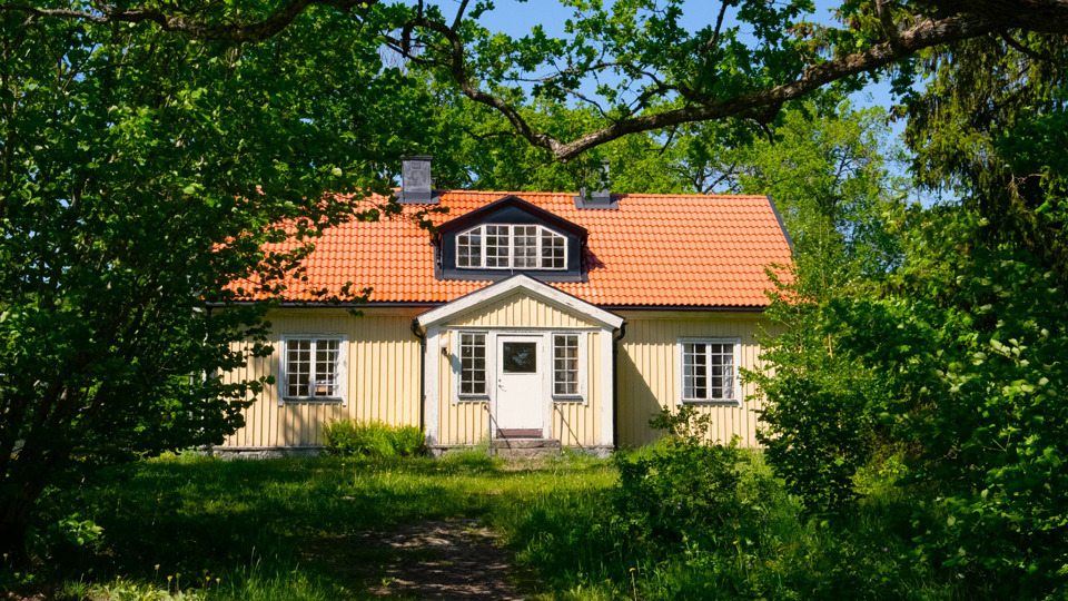 Ett gult trähus i två plan. Huset är inbäddat i grönska.