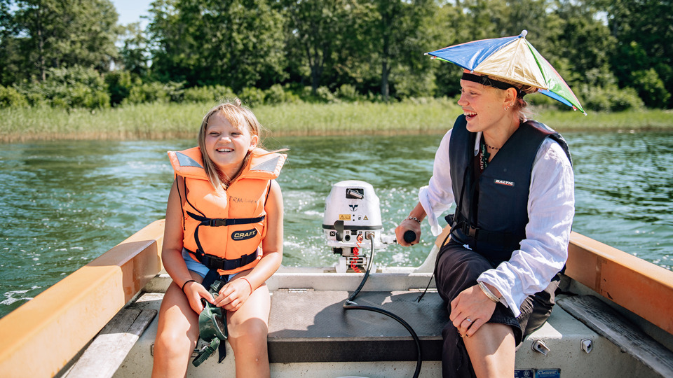 Ett barn och en kolloledare sitter i aktern på en liten båt och styr ut från land.