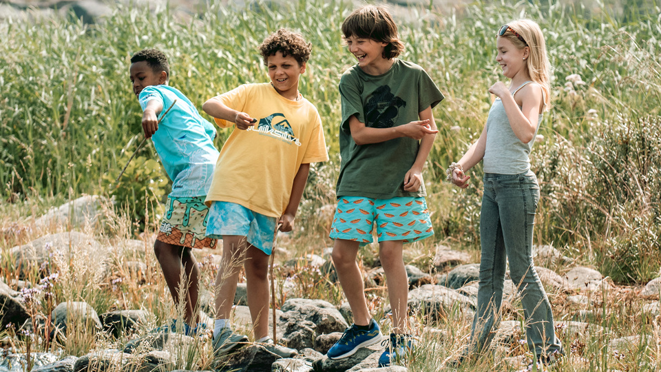 Fyra barn leker och klättrar på stenar vid en strand.