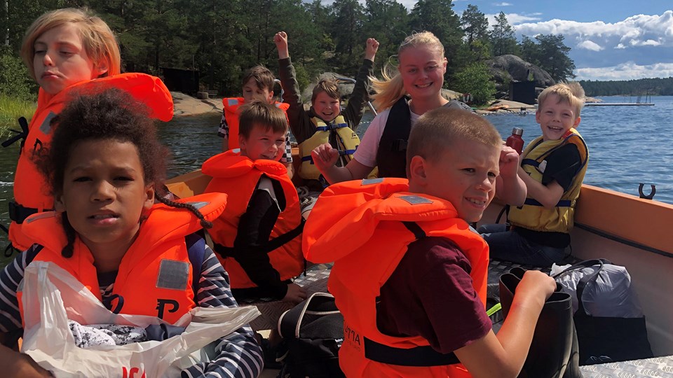 En grupp med glada barn i flytvästar på en båt.