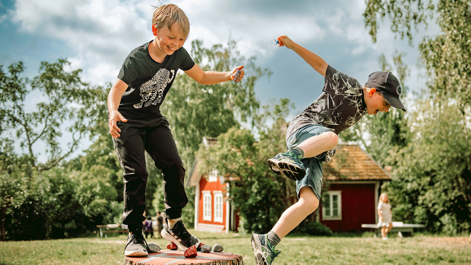 Två barn balanserar och hoppar från en stubbe.