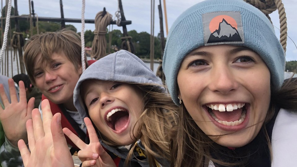 Tre glada barn ombord på ett fartyg. De vinkar in mot kameran.