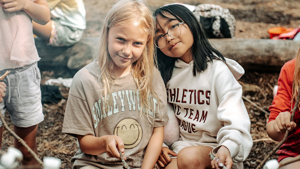 Barn sitter utomhus och grillar marshmallows.