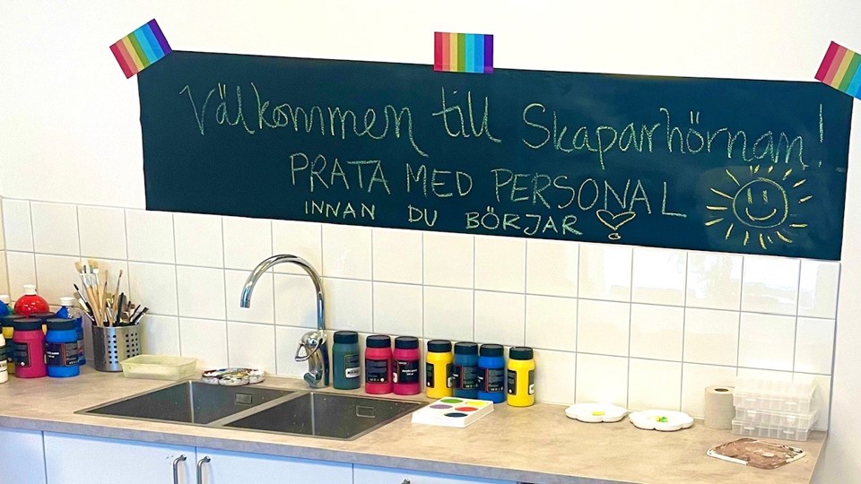 Skylt där det står "Välkommen till Skaparhörnan" över en diskbänk med målarfärger, penslar med mera. 