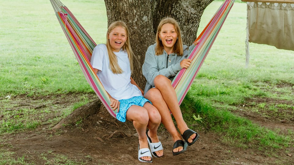 Två glada barn sitter i en hängmatta.