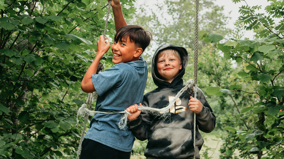 Två barn hänger i klätterrep i skogen.