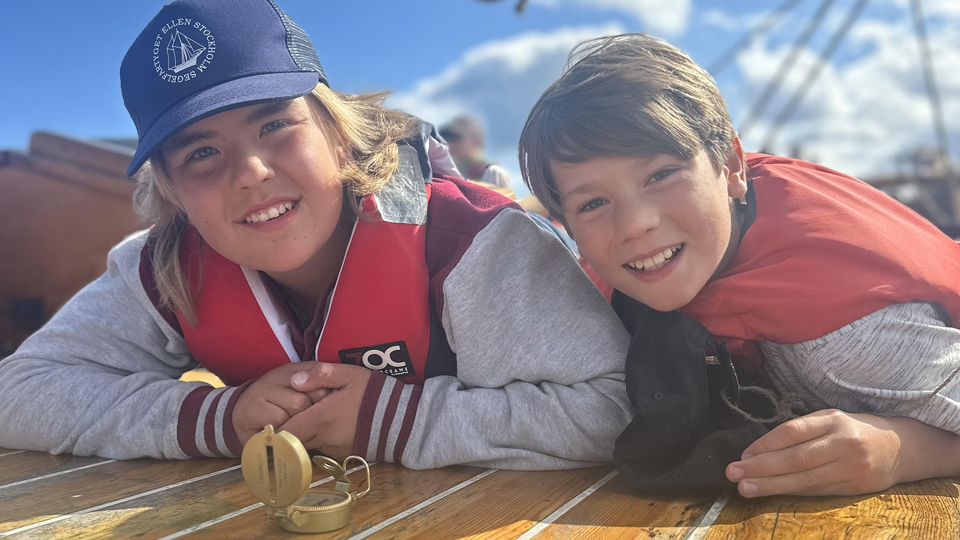 Två barn i flytvästar lutar sig mot fartygets däck och ler in i kameran.