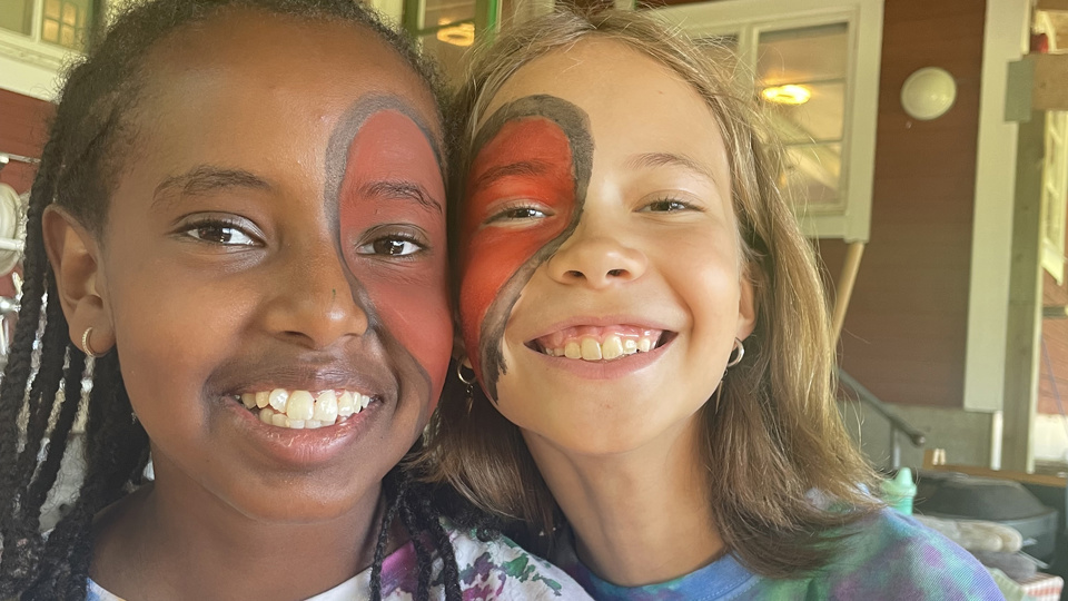 Två barn med målade hjärtan i ansiktet ler in i kameran.