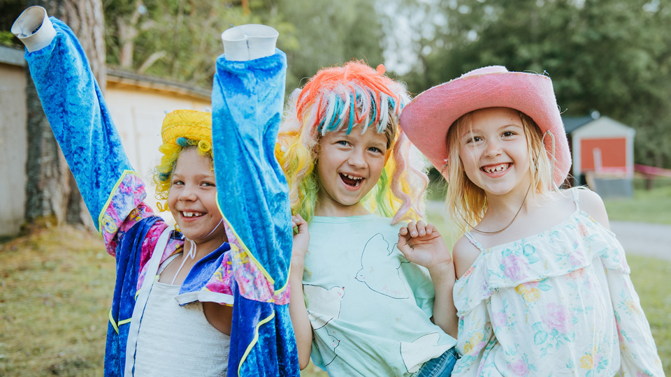 Tre barn som har klätt ut sig skrattar och tittar in i kameran.
