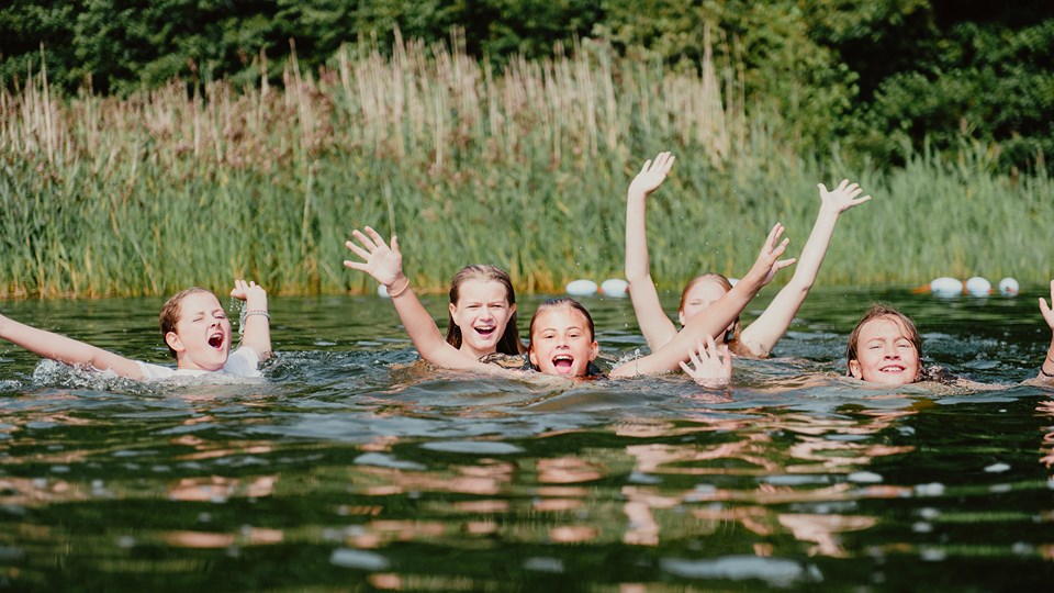 Fem ungdomar badar, skrattar och sträcker upp händerna ur vattnet.