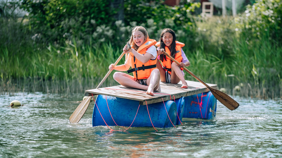 Två barn paddlar på en flotte.