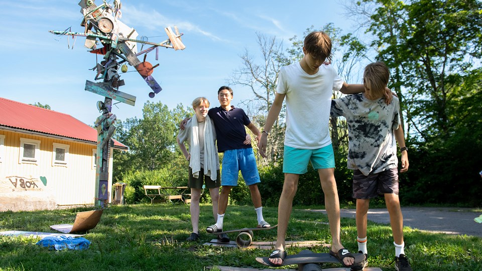 Fyra barn gör balanslekar med skateboardbrädor i en trädgård.