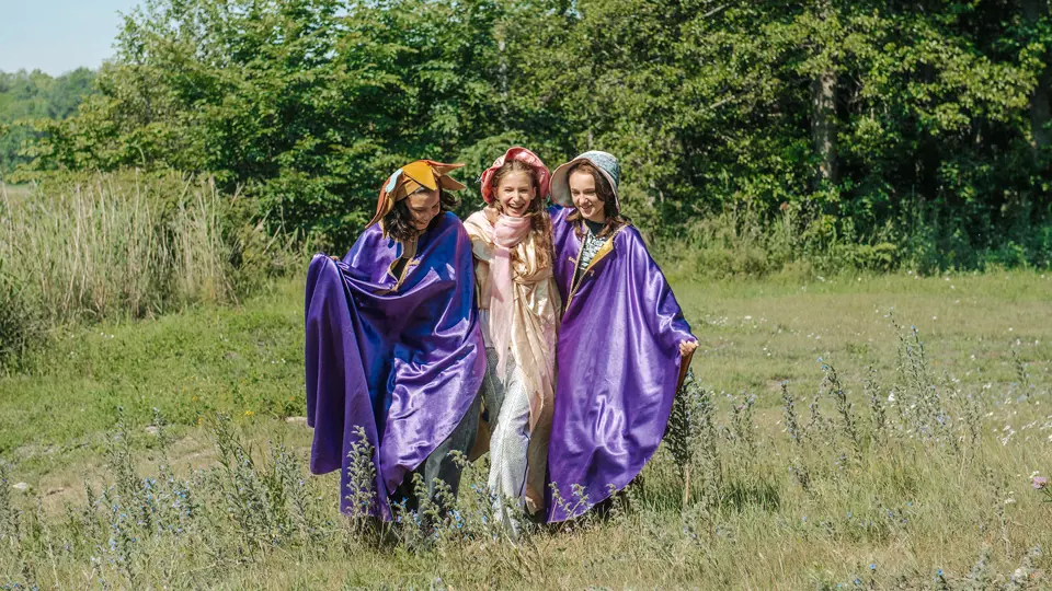 Tre glada, utklädda barn står ute på en äng.