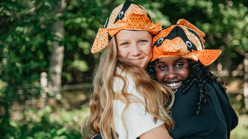 Två glada barn i roliga hattar kramar om varandra.