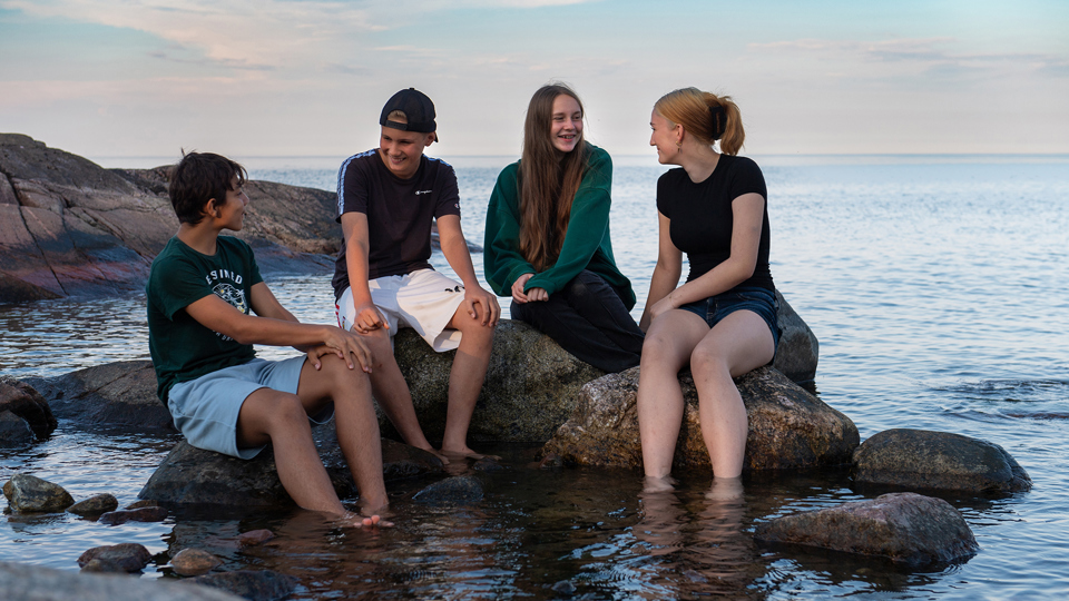 Fyra ungdomar sitter på klippor ute i vattnet.